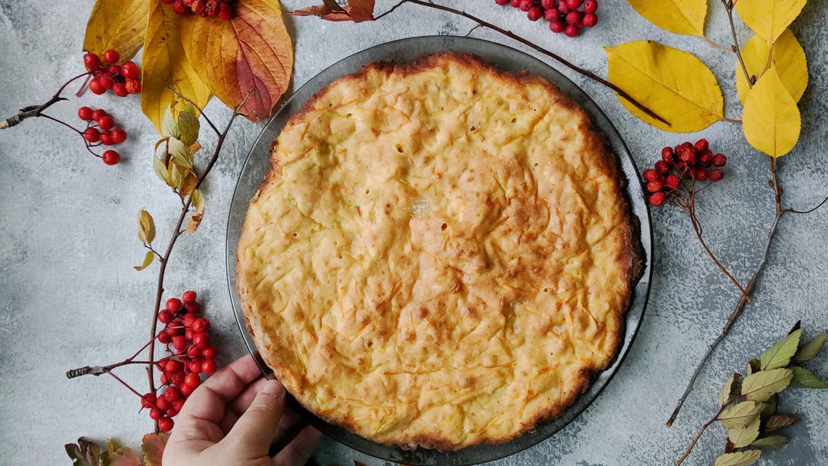 Freshly baked pie surrounded by autumn leaves and rowanberries on a rustic table.